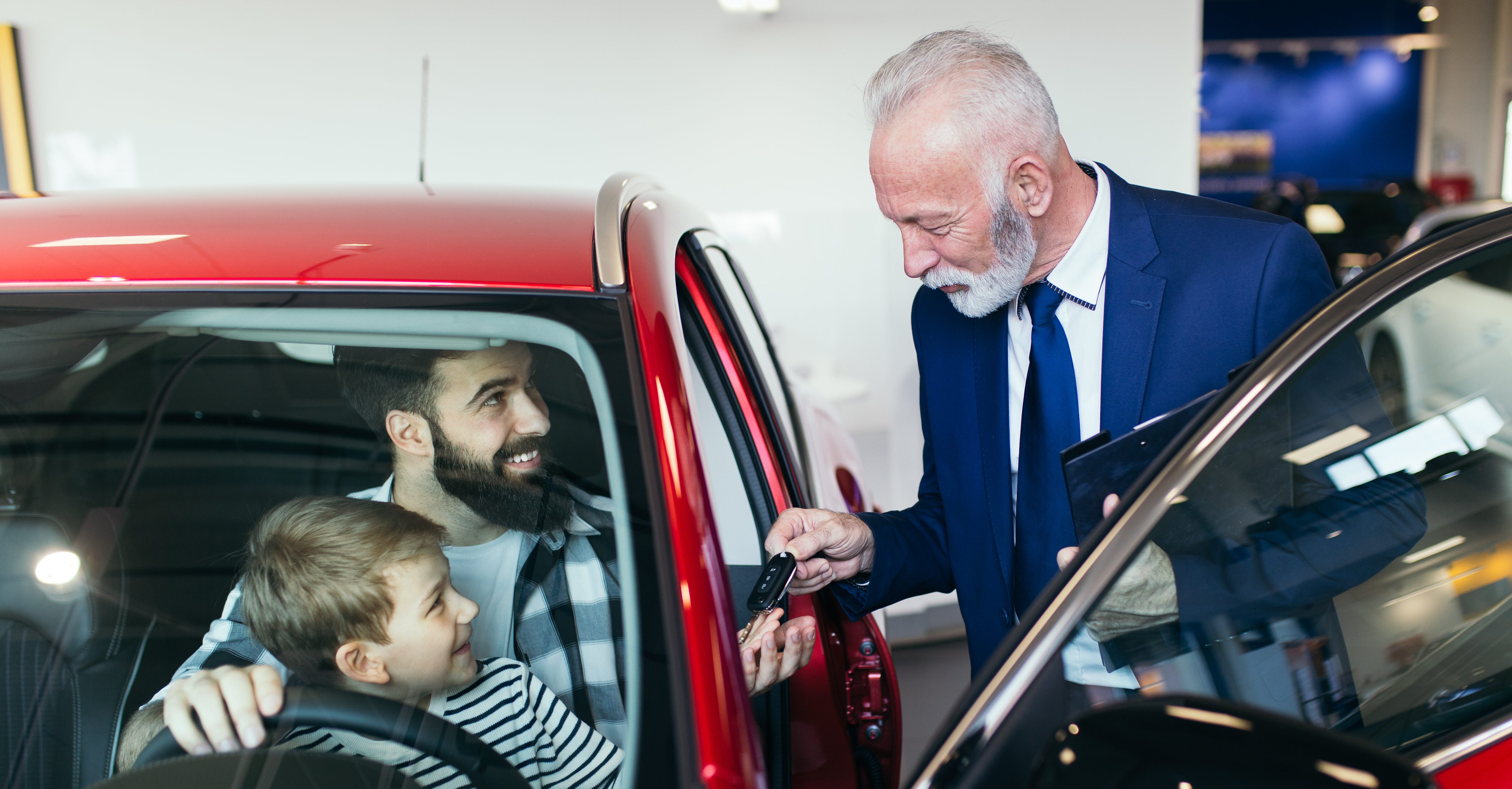 Father and son talking with a salesman about buying a new car at the car showroom.