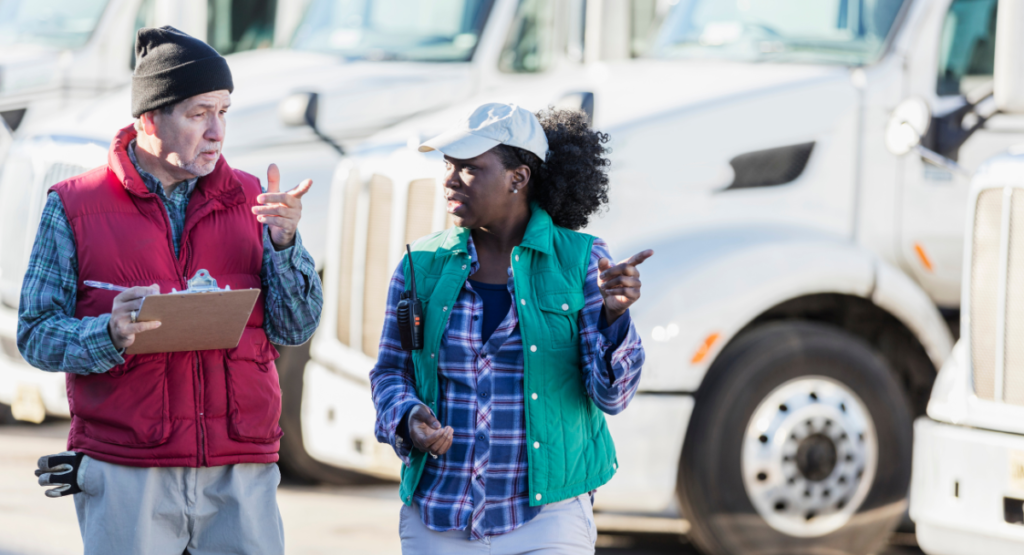 A man holding a clipboard and a woman talking in front of a fleet of trucks